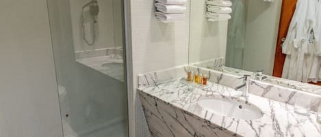 Un baño con ducha de vidrio, lavamanos de mármol y un espejo grande.