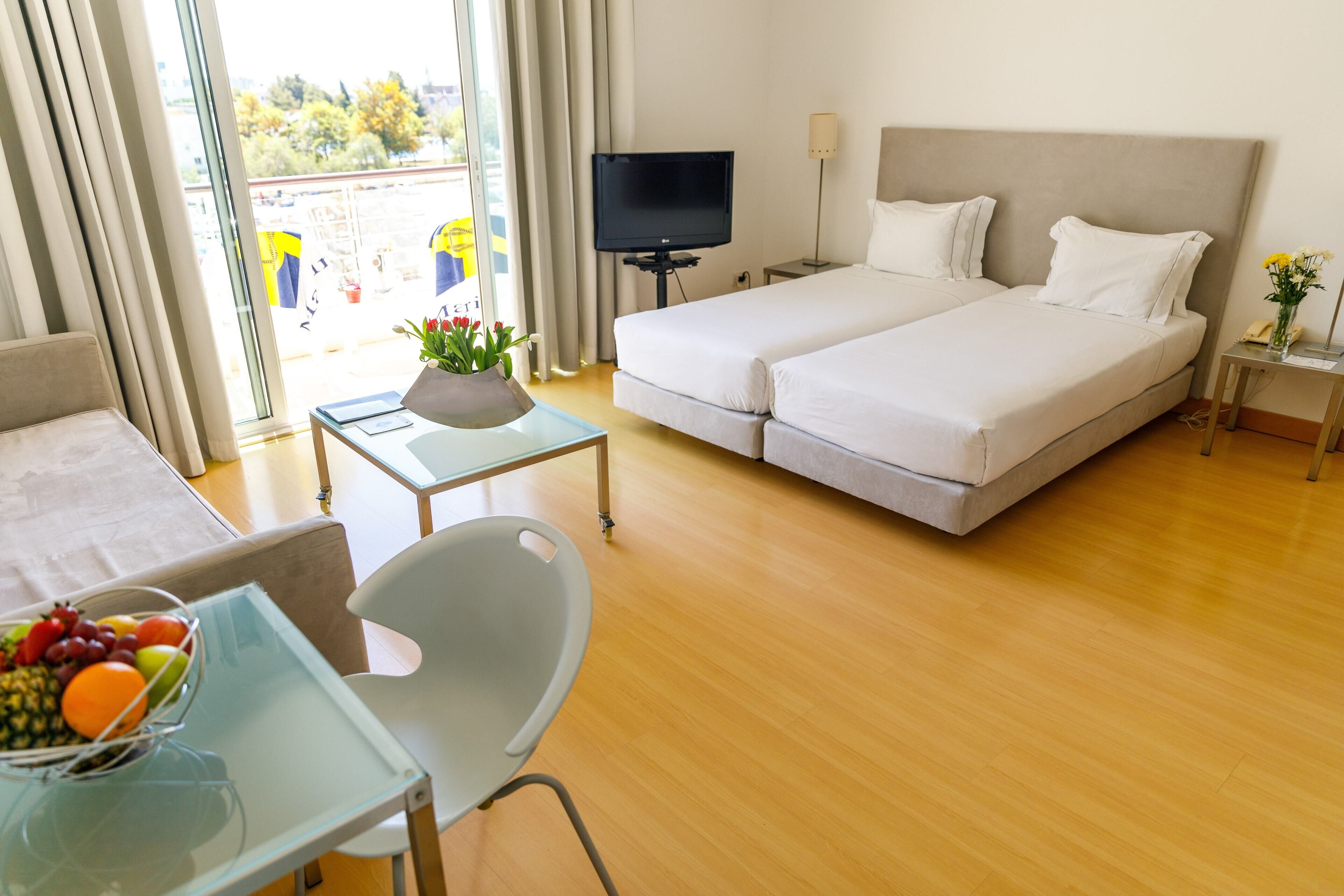 A hotel room with a bed, a desk with a chair, a TV, and a window with curtains.