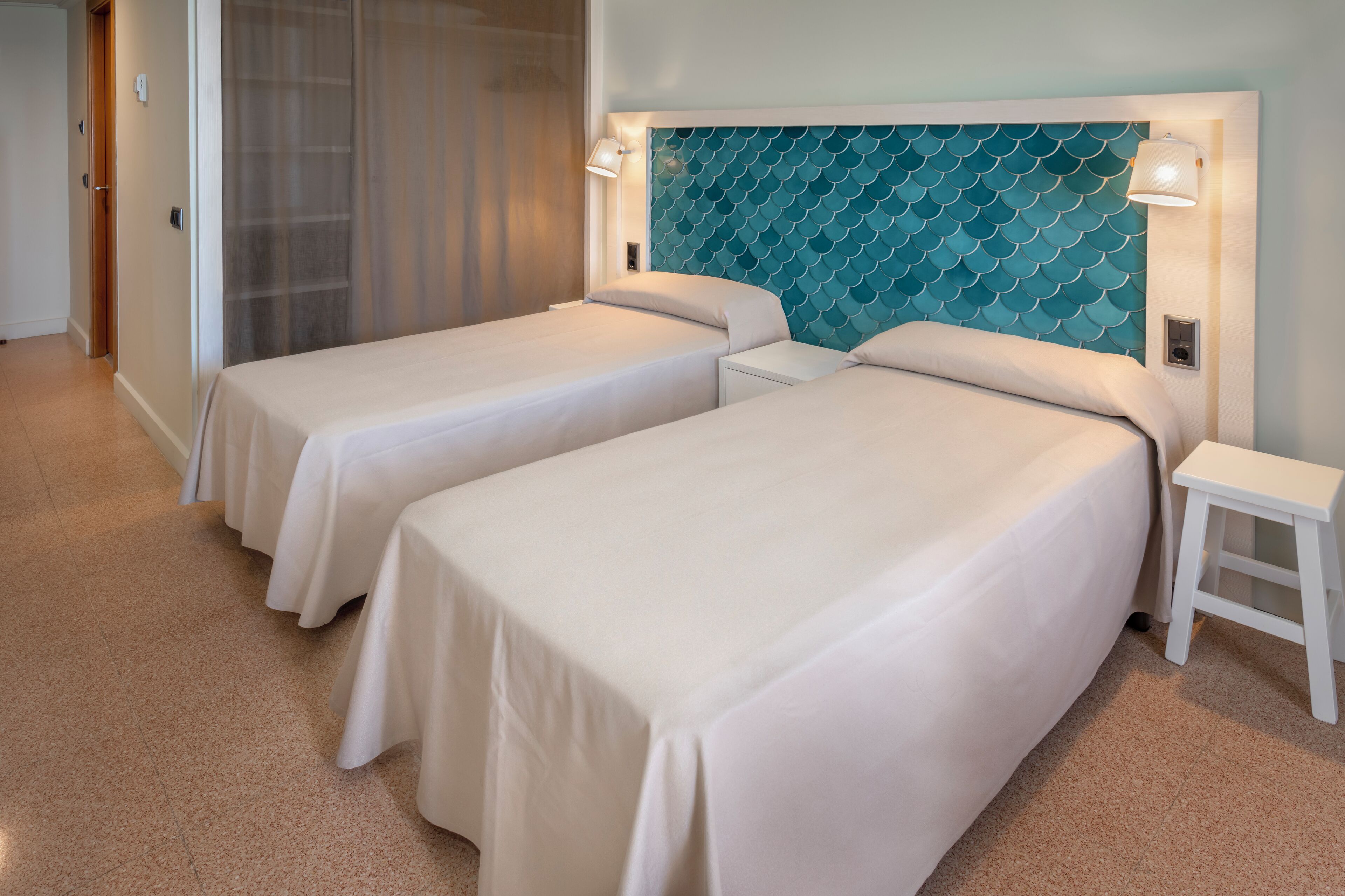 Une chambre d’hôtel avec deux lits simples, une grande tête de lit de couleur turquoise et une table de chevet blanche.