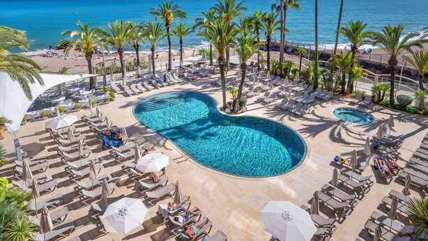 A pool area with lounge chairs, palm trees, and a view of the beach and ocean.