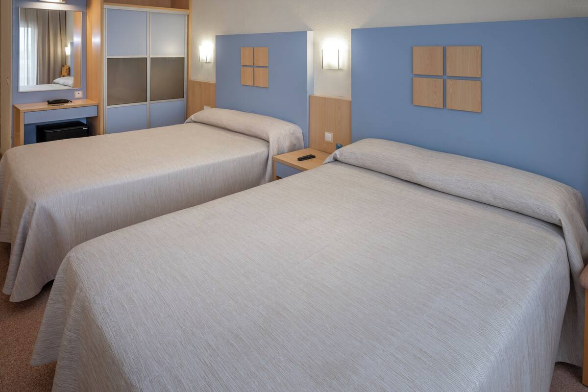 Een hotelkamer met twee bedden, een bureau, een spiegel en wandlampen.