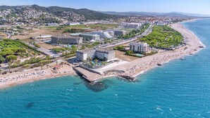 An aerial view of a coastal hotel with multiple buildings, a beach, and a promenade along the water.