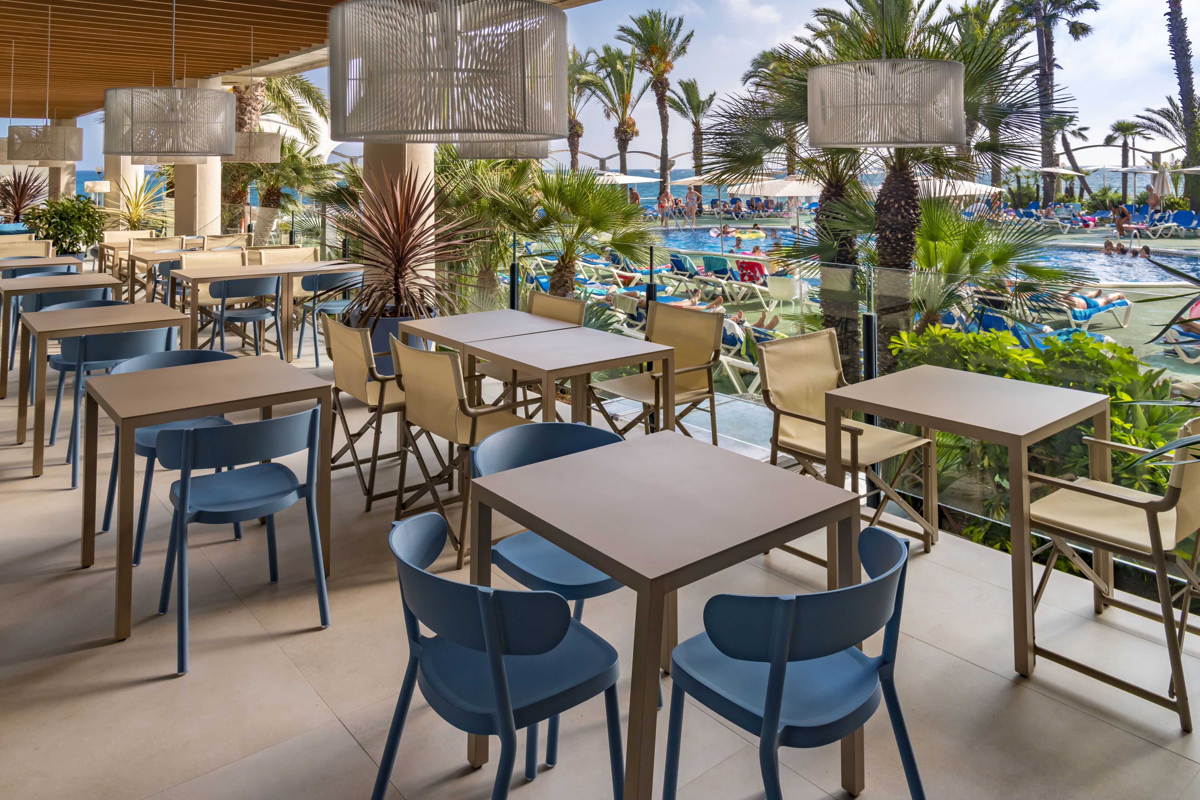 Un espace aménagé au bord de la piscine, avec des tables et des chaises, donnant sur une piscine équipée de transats et de parasols.