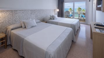 A hotel room with two beds, a balcony with a view of the sea, and a small desk with a chair.