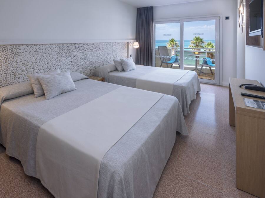 A hotel room with two beds, a balcony with a view of the sea, and a small desk with a chair.