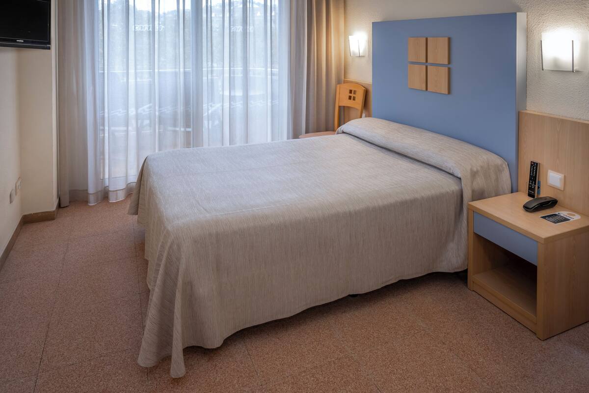 Een hotelkamer met een bed, nachtkastje, lamp en een raam met gordijnen.