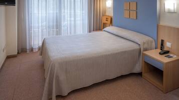 Une chambre d’hôtel avec un lit, une table de chevet, une lampe et une fenêtre avec des rideaux.