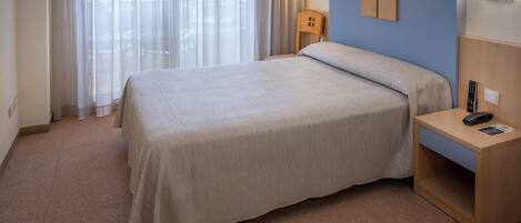 Une chambre d’hôtel avec un lit, une table de chevet, une lampe et une fenêtre avec des rideaux.