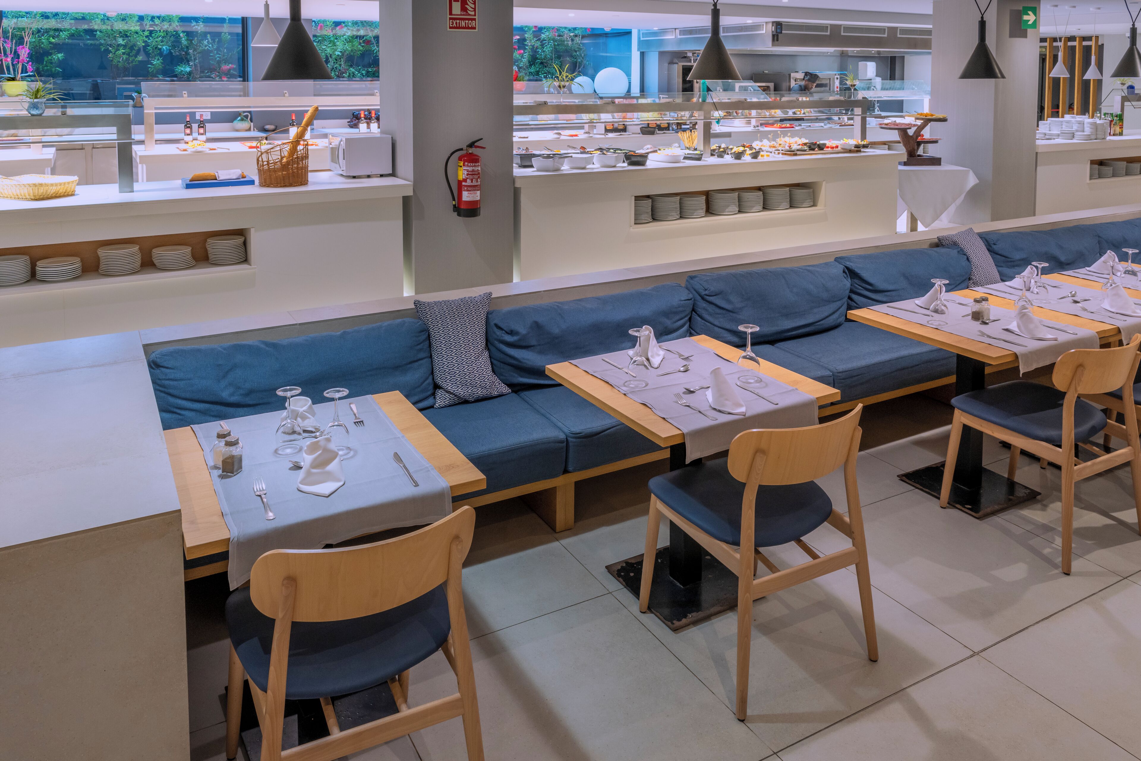 A modern dining area with a long blue sofa and wooden tables set for dining.