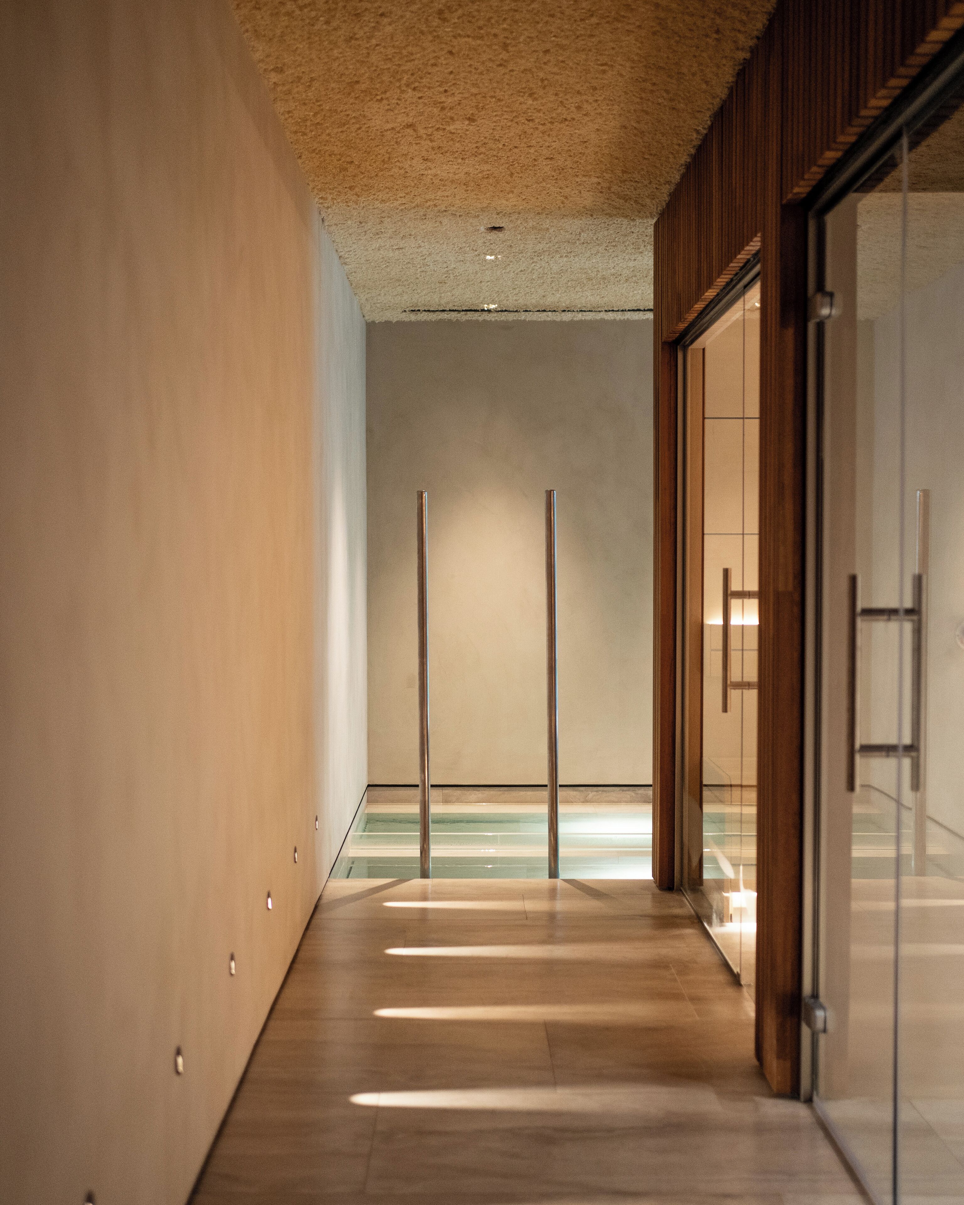 A corridor with a wooden floor, a glass door on the right, and a ceiling with a textured finish.