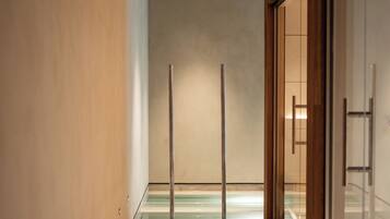 A corridor with a wooden floor, a glass door on the right, and a ceiling with a textured finish.