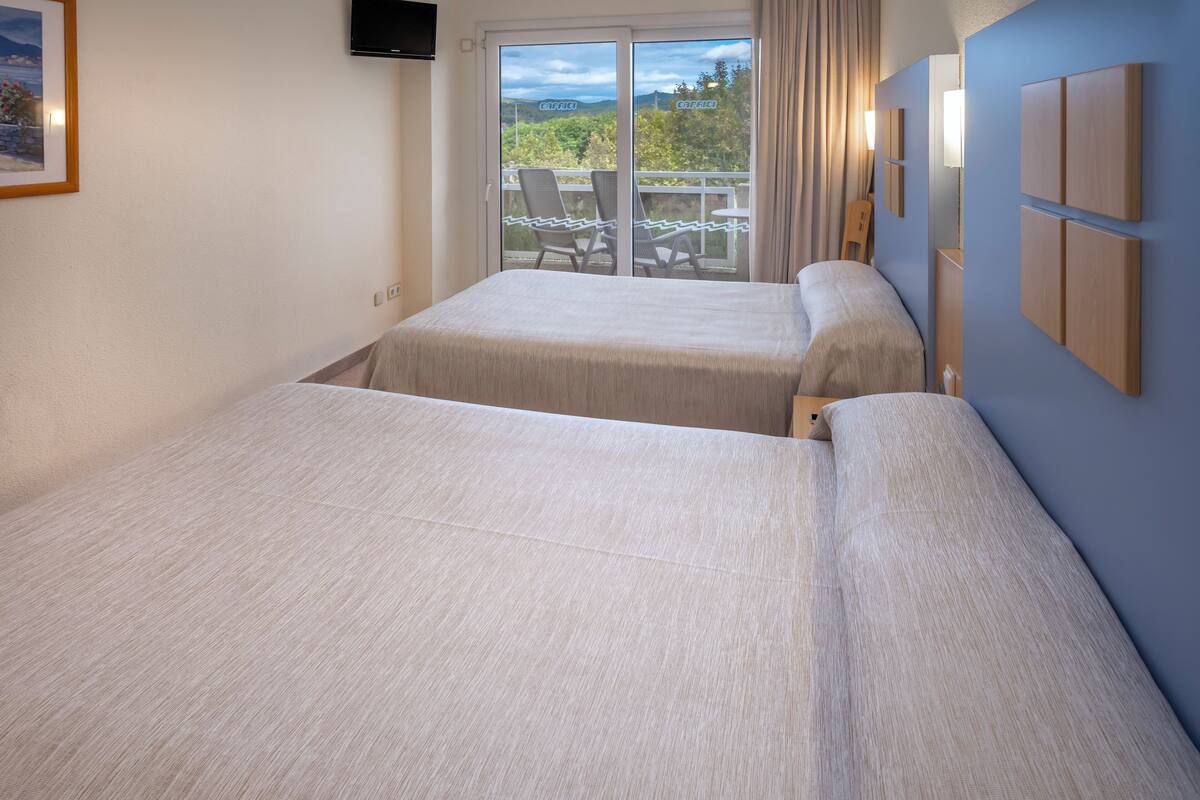 Een hotelkamer met twee bedden, een balkon met stoelen en een aan de muur bevestigde televisie.