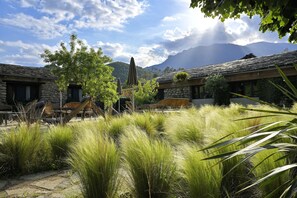 Un albergue rústico con paredes de piedra, asientos exteriores y vistas a las montañas.