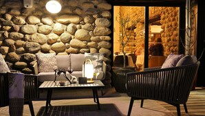 Um interior acolhedor com parede de pedra, um sofá, uma mesa com uma taça de vinho e um abajur.