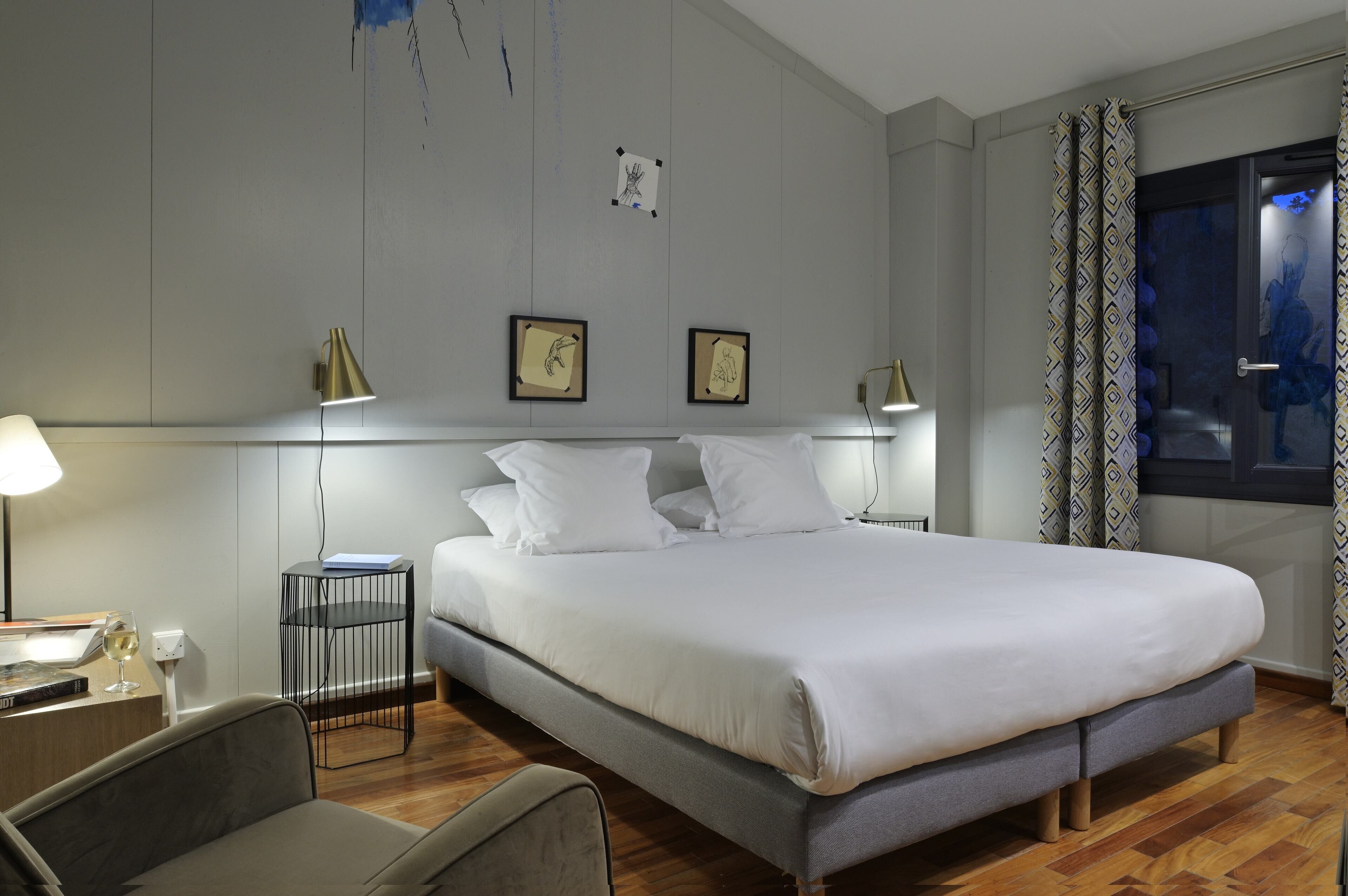 Un dormitorio moderno con una cama grande, dos lámparas de noche, una mesita auxiliar y una silla.