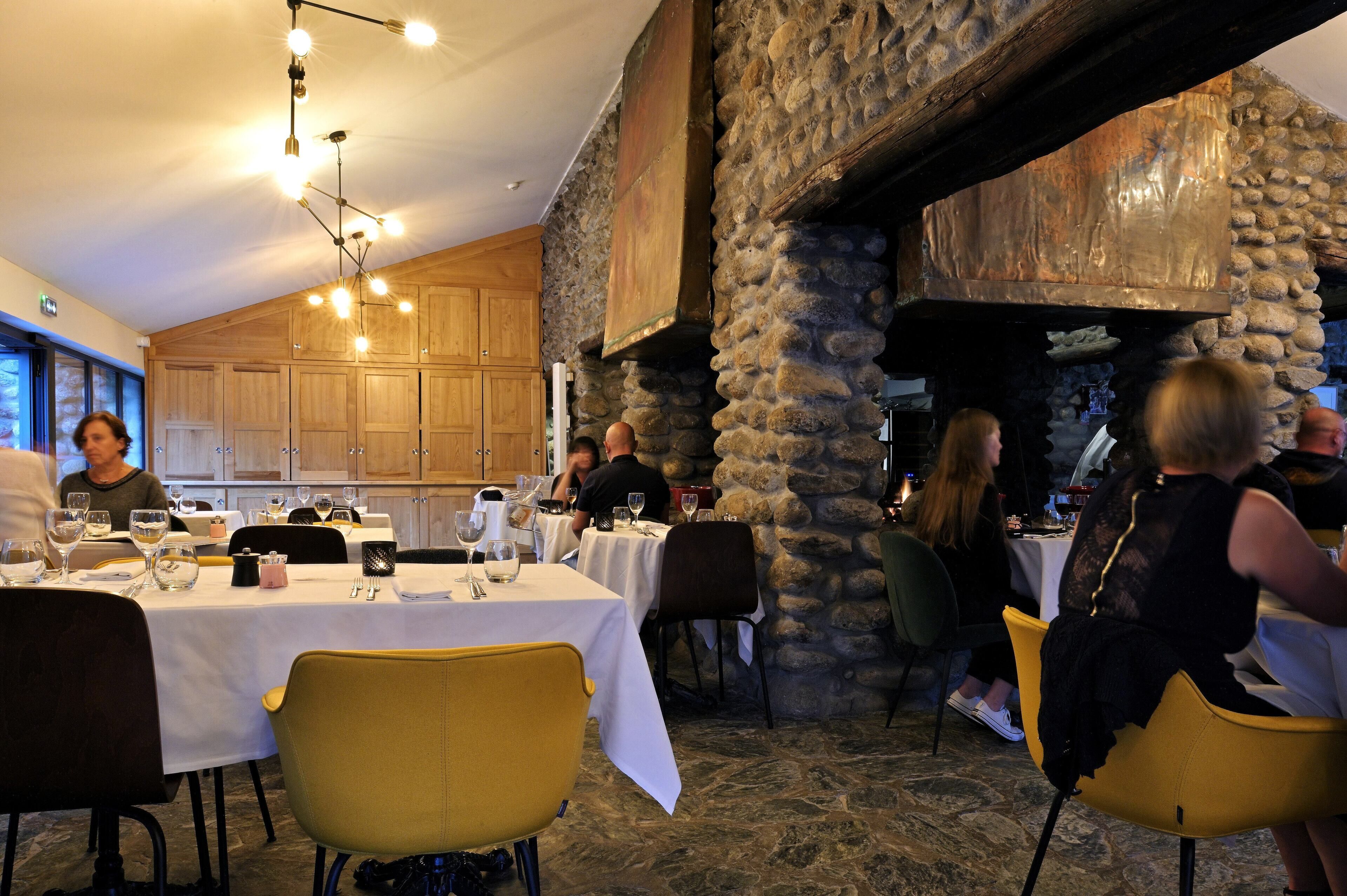 Ein Restaurant mit Steinwänden und Holzsäcken, Tische sind mit weißen Tischdecken und gelben Stühlen gedeckt.