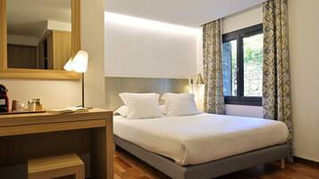A neatly made bed with white bedding, a wooden desk with a lamp, and a large mirror on the wall.