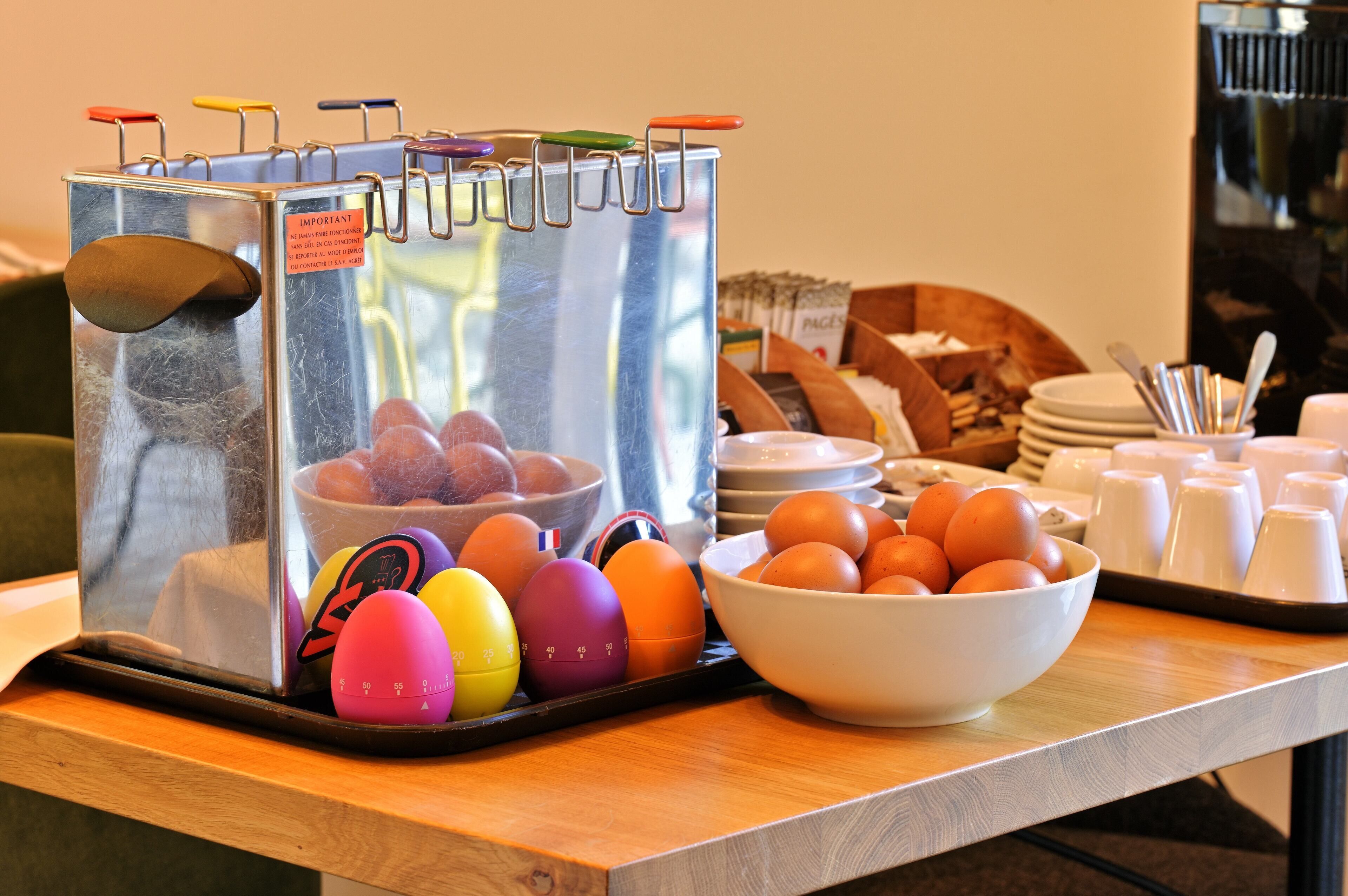 Montaje de un bufé de desayuno con una cafetera, un bol de huevos y diversas opciones para el desayuno sobre una mesa de madera.