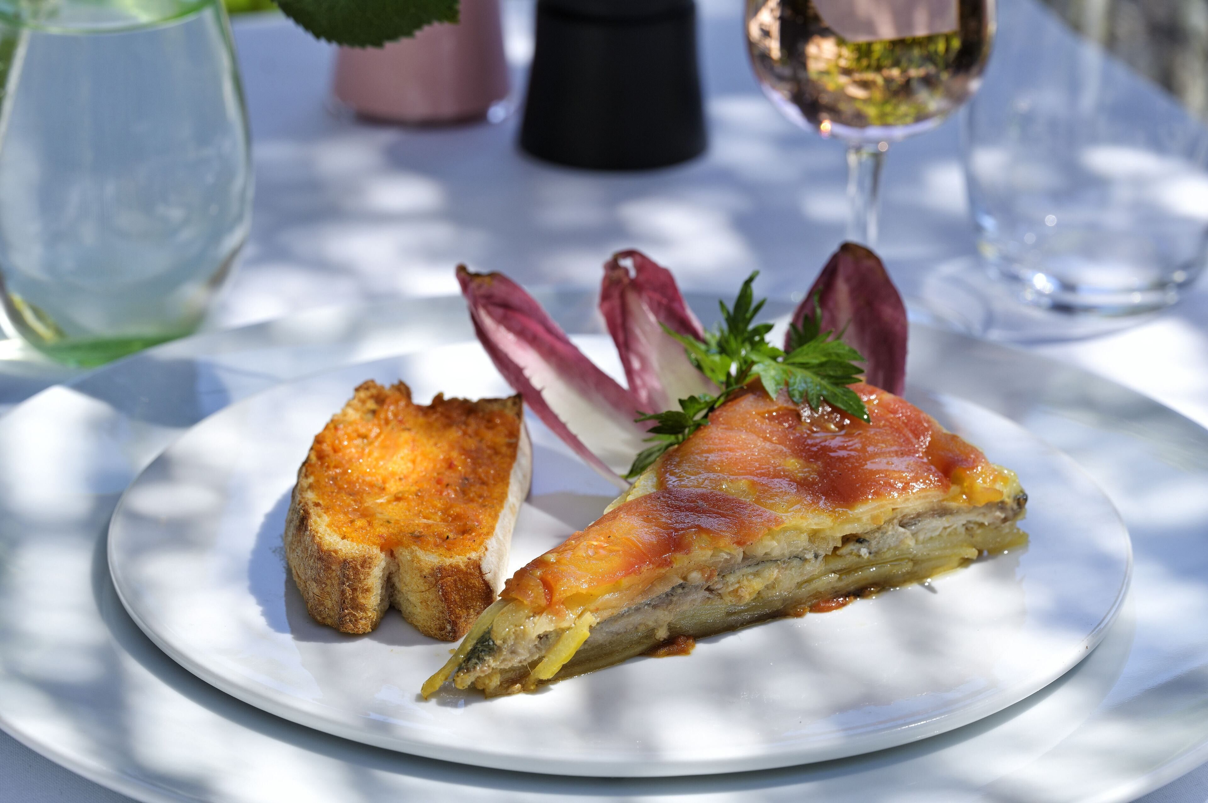 Une assiette blanche sur laquelle on voit une part de quiche et une tranche de pain grillé.
