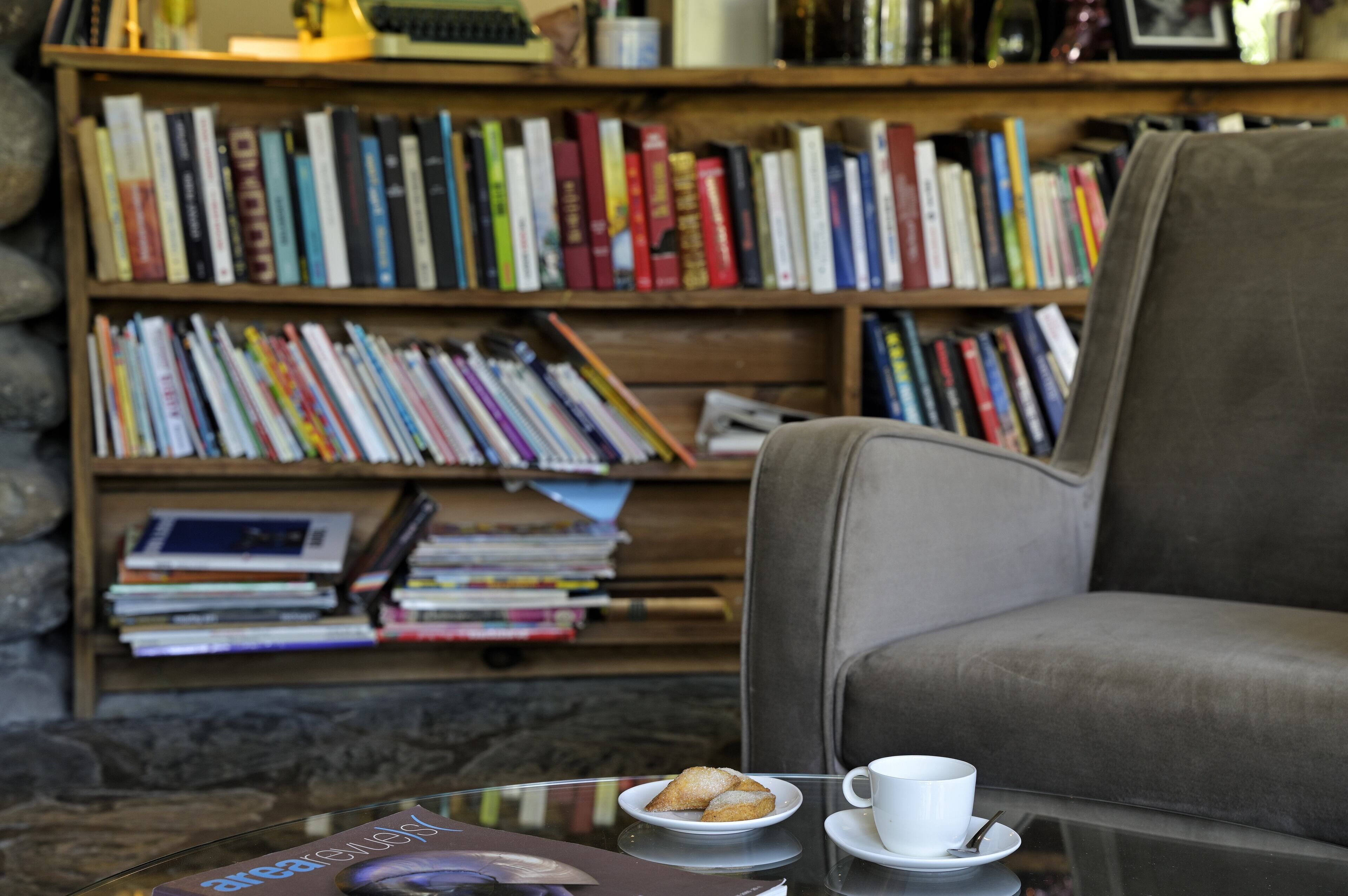 A cozy reading area with a leather armchair, a glass coffee table with a cup and a plate of cookies, and a bookshelf filled with books.