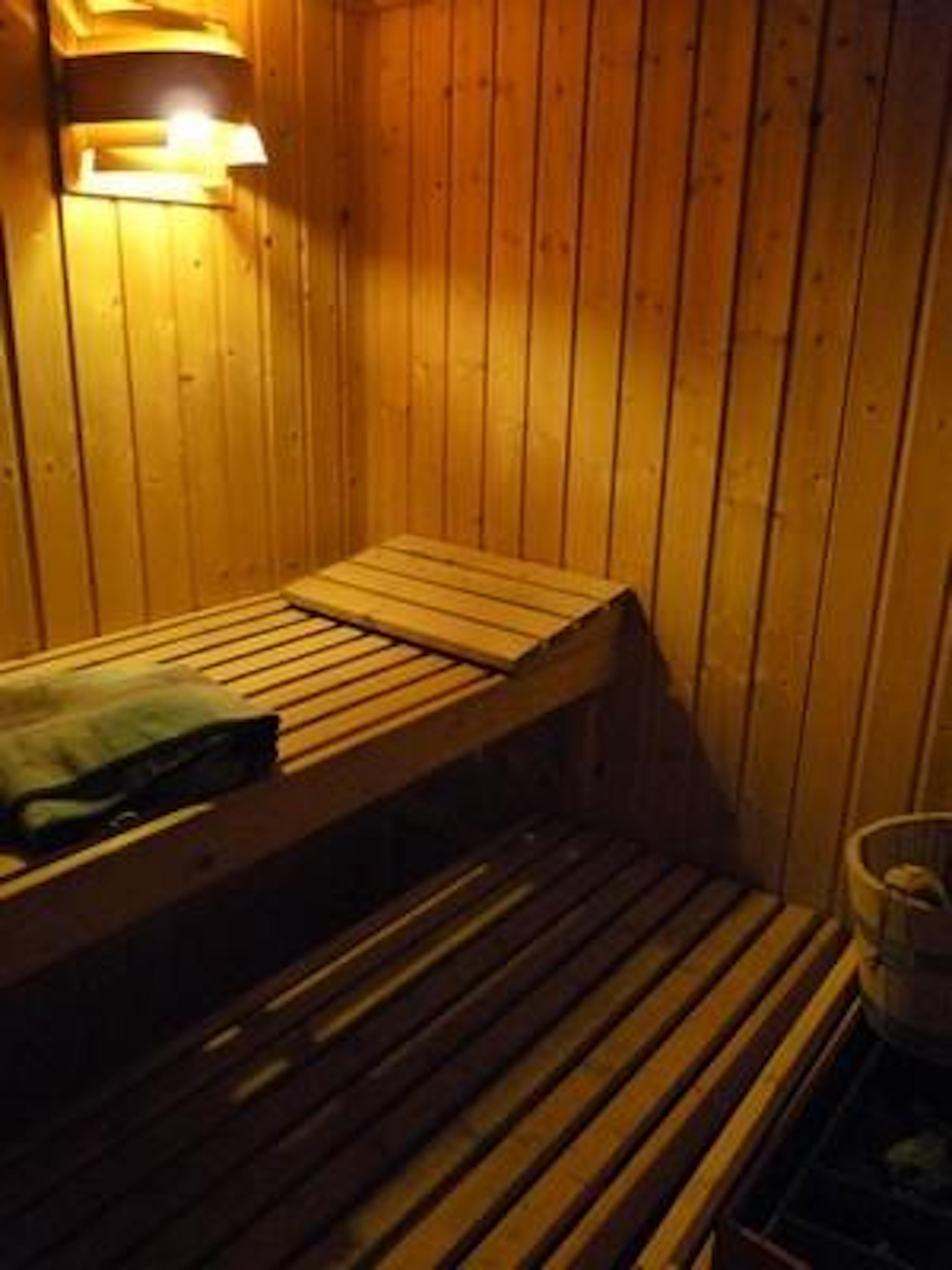 A wooden sauna with a bench and a small container, likely for water or towels.