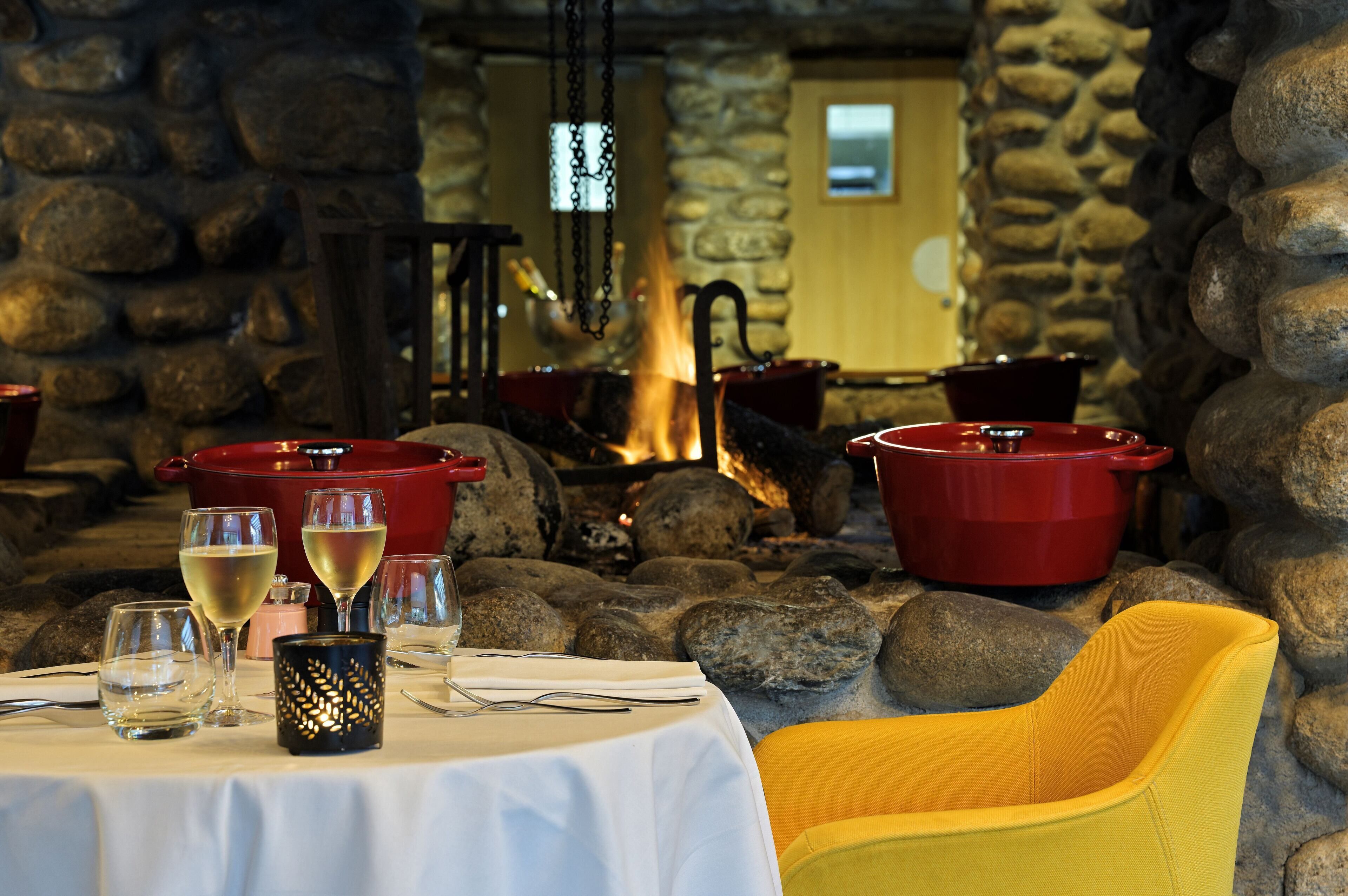 Un coin repas aux murs de pierre, avec une table dressée pour deux personnes, agrémentée de verres à vin et d’un chandelier.
