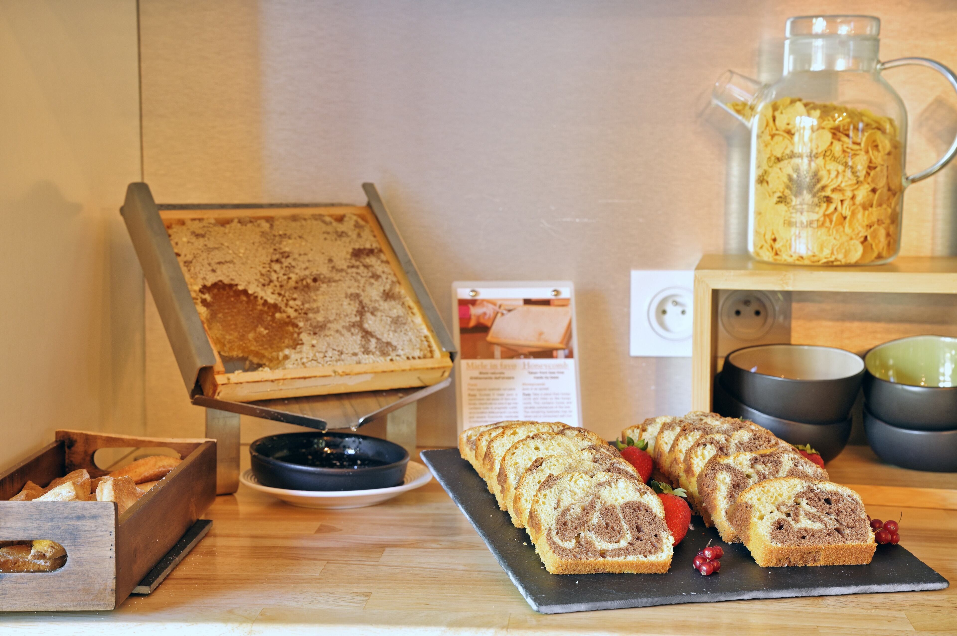 Mostrador de panadería con pan, pasteles, una cafetera y un letrero con recetas.
