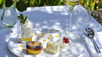 Un plato de postres con varios dulces y una copa de vino blanco sobre una mesa al aire libre.