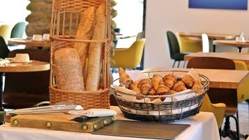 A breakfast setting with bread and croissants on a table, surrounded by chairs and tables in a dining area.