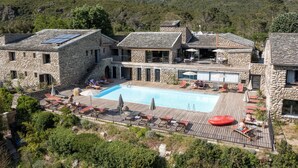Um edifício de pedra com piscina, área de estar ao ar livre e montanhas ao fundo.