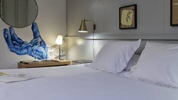 Hotelkamer met een bed, nachtkastje met lamp, muur met een grote blauwe handafdruk muurschildering en een ingelijste foto aan de muur.