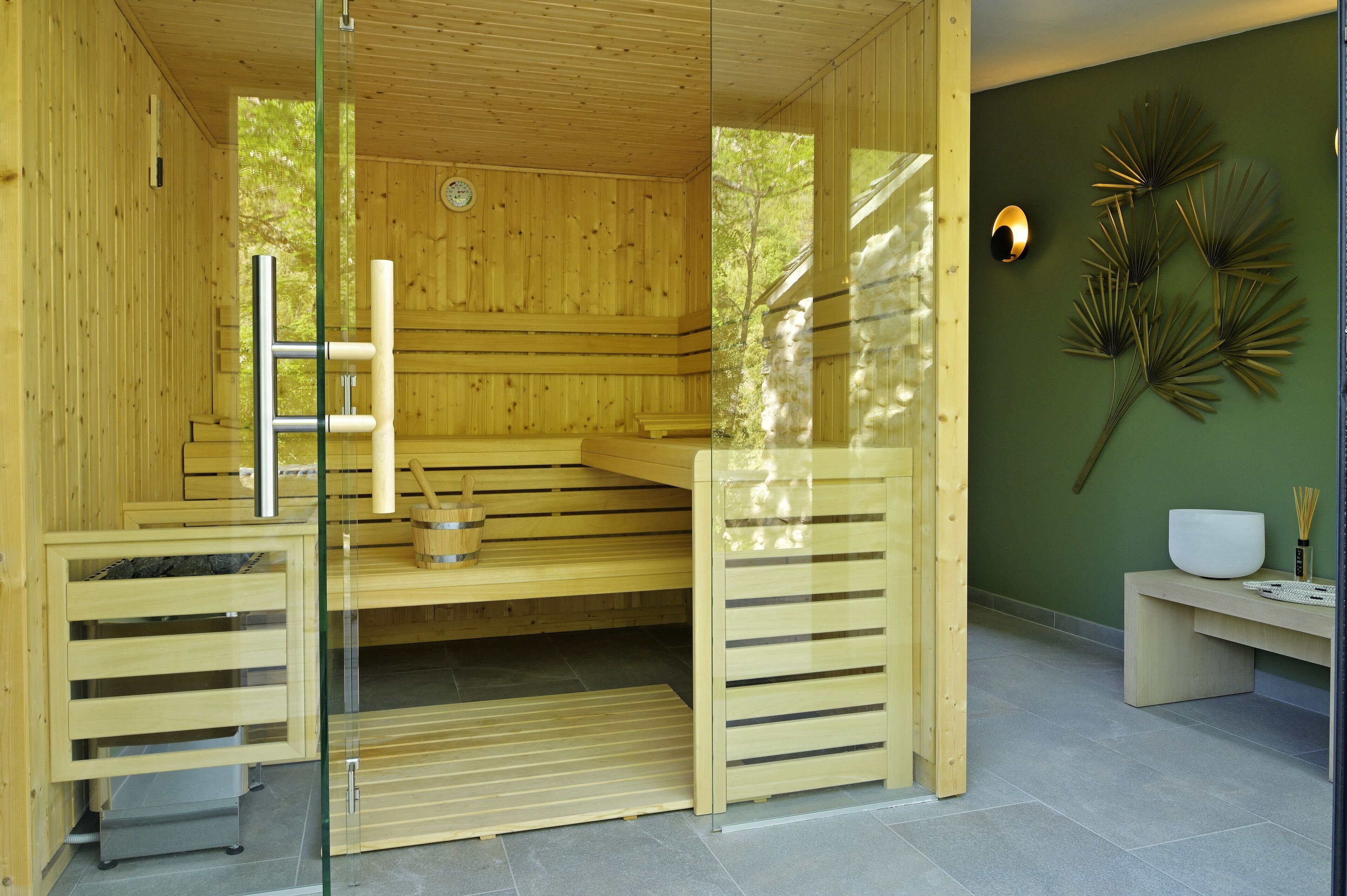 A wooden sauna with glass doors, a bench, and a wall-mounted heater.