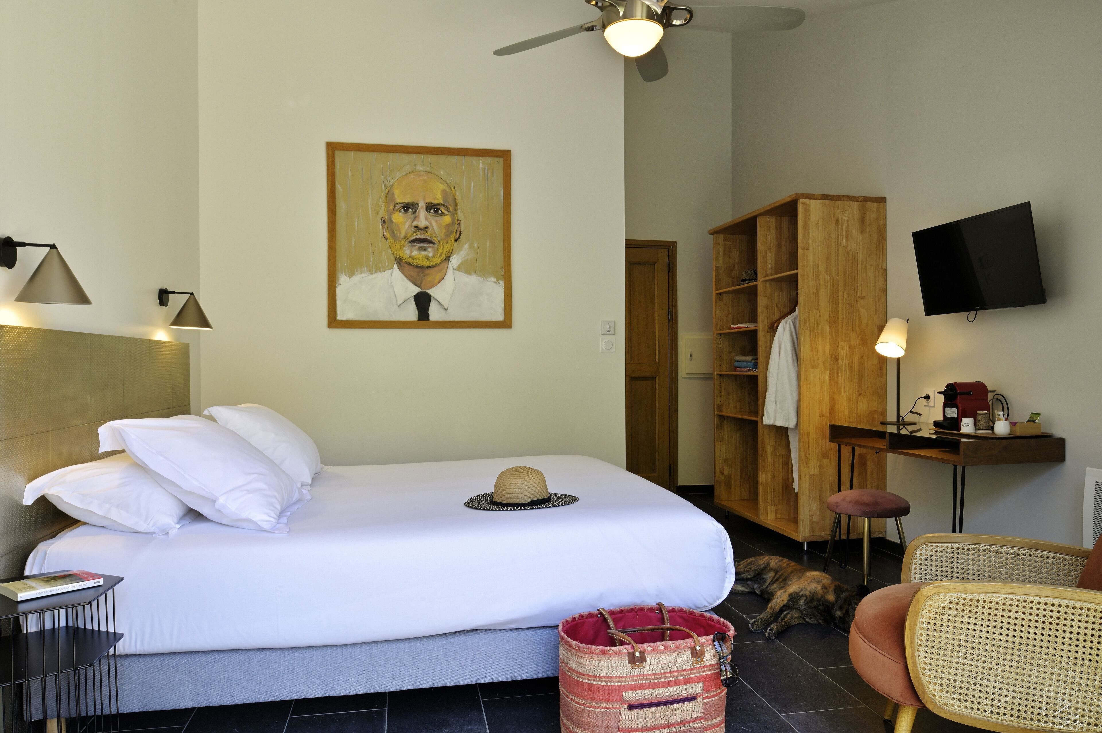 A hotel room with a bed, a wooden wardrobe, a television, and a desk with a lamp.