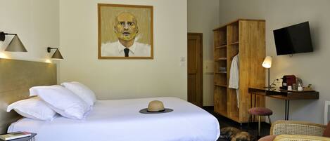 A hotel room with a bed, a wooden wardrobe, a television, and a desk with a lamp.