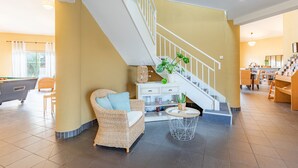 A spacious living area with a pool table, a wicker sofa, a staircase, and a dining area.