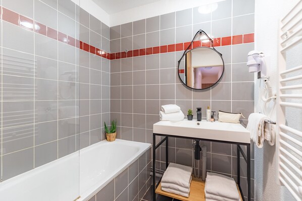 A modern bathroom with a bathtub, a sink with a mirror, a towel rack, and a small potted plant. - Appart'City Classic Toulouse Saint Simon (Toulouse)