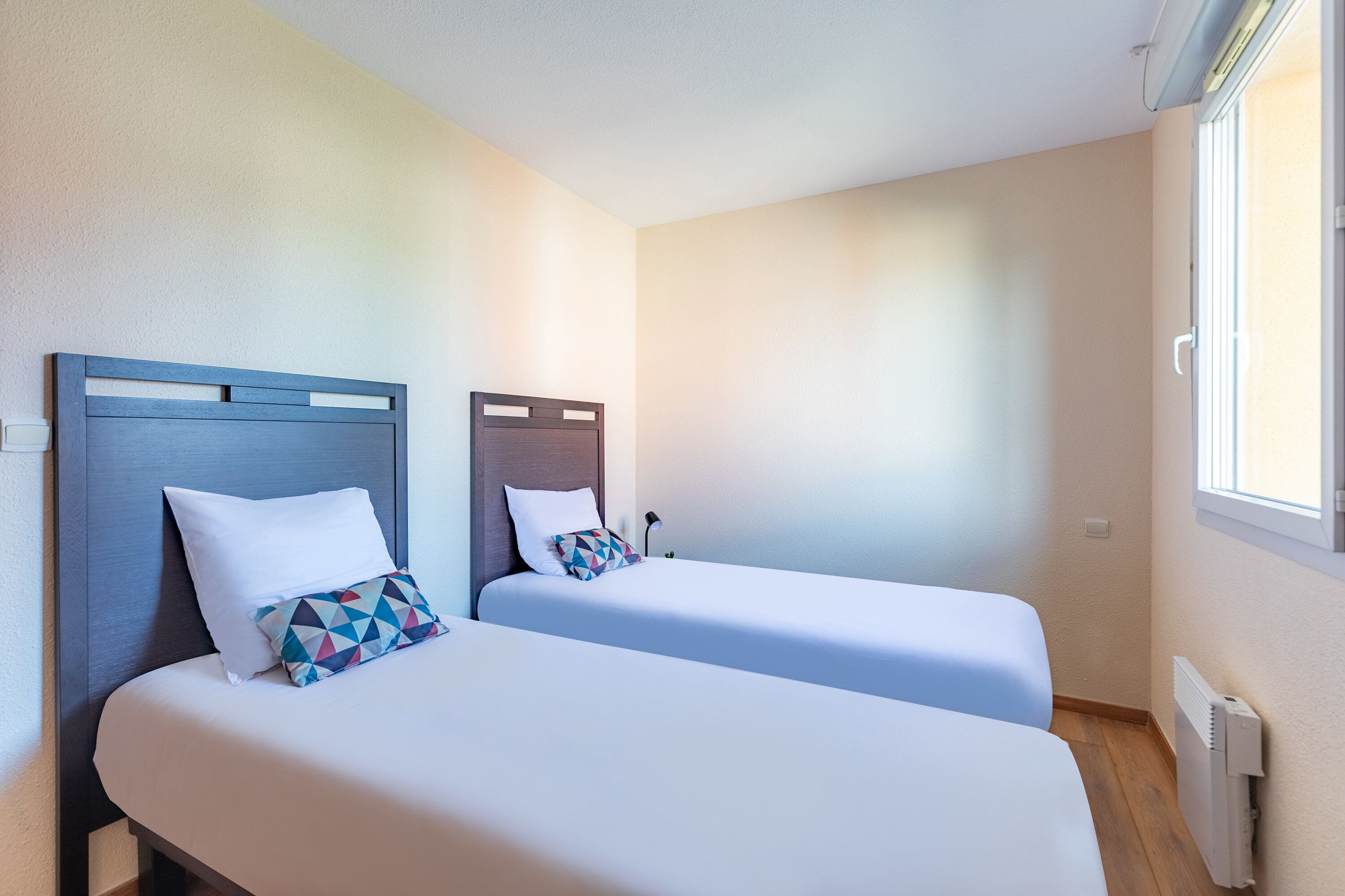 A hotel room with two single beds, each with a wooden headboard and white bedding.
