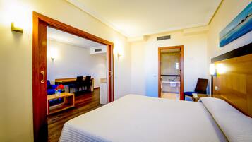 Habitación de hotel con una cama grande, un cabecero de madera, un escritorio con una silla y una pequeña zona de estar con un sofá y una mesa.