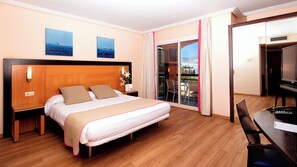 A hotel room with a wooden bed, a desk with a chair, a TV, and a balcony with a view. - Hotel Bonalba Alicante (Mutxamel)
