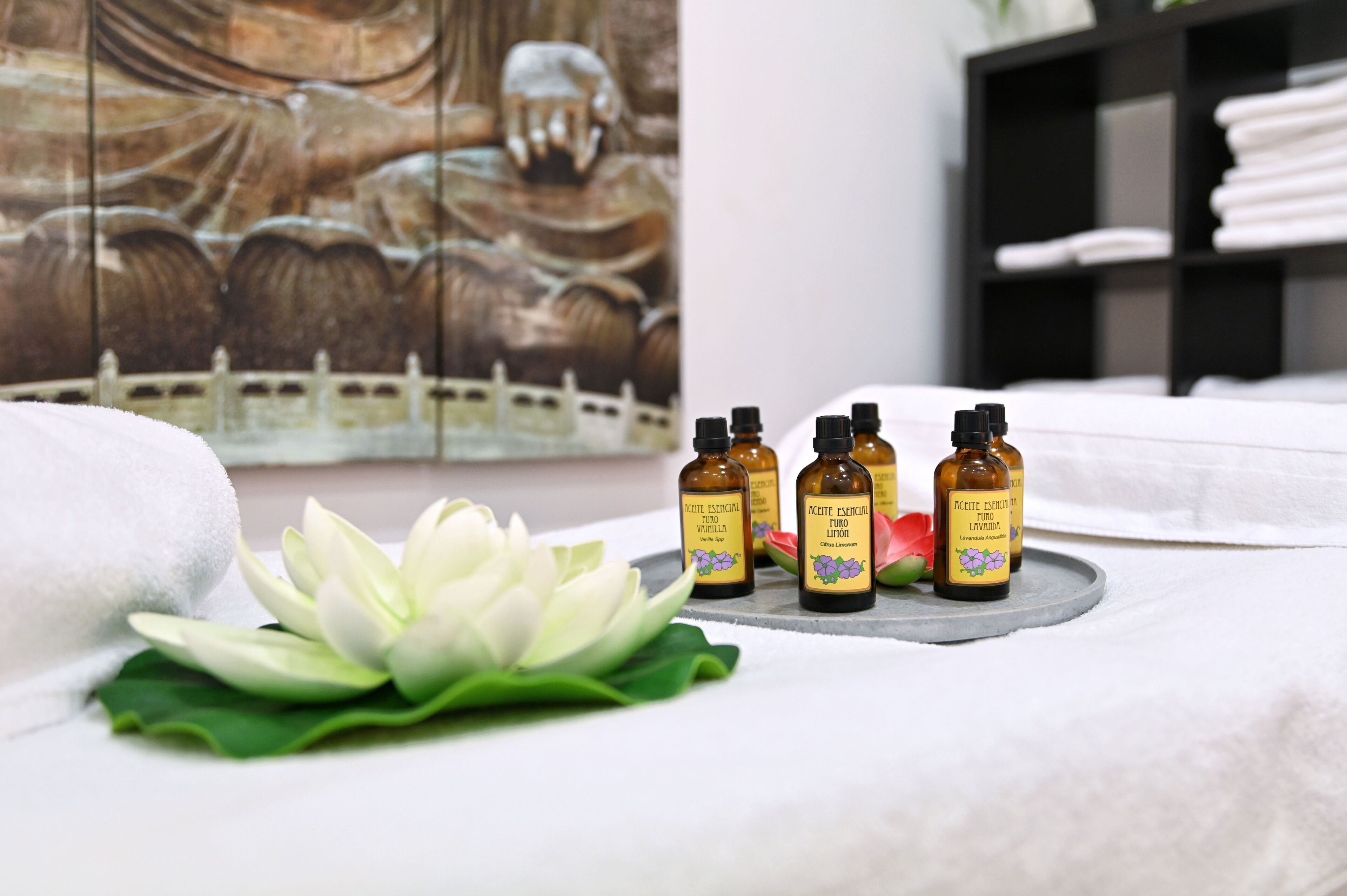 A spa setting with a lotus flower, a towel, and essential oil bottles on a tray.