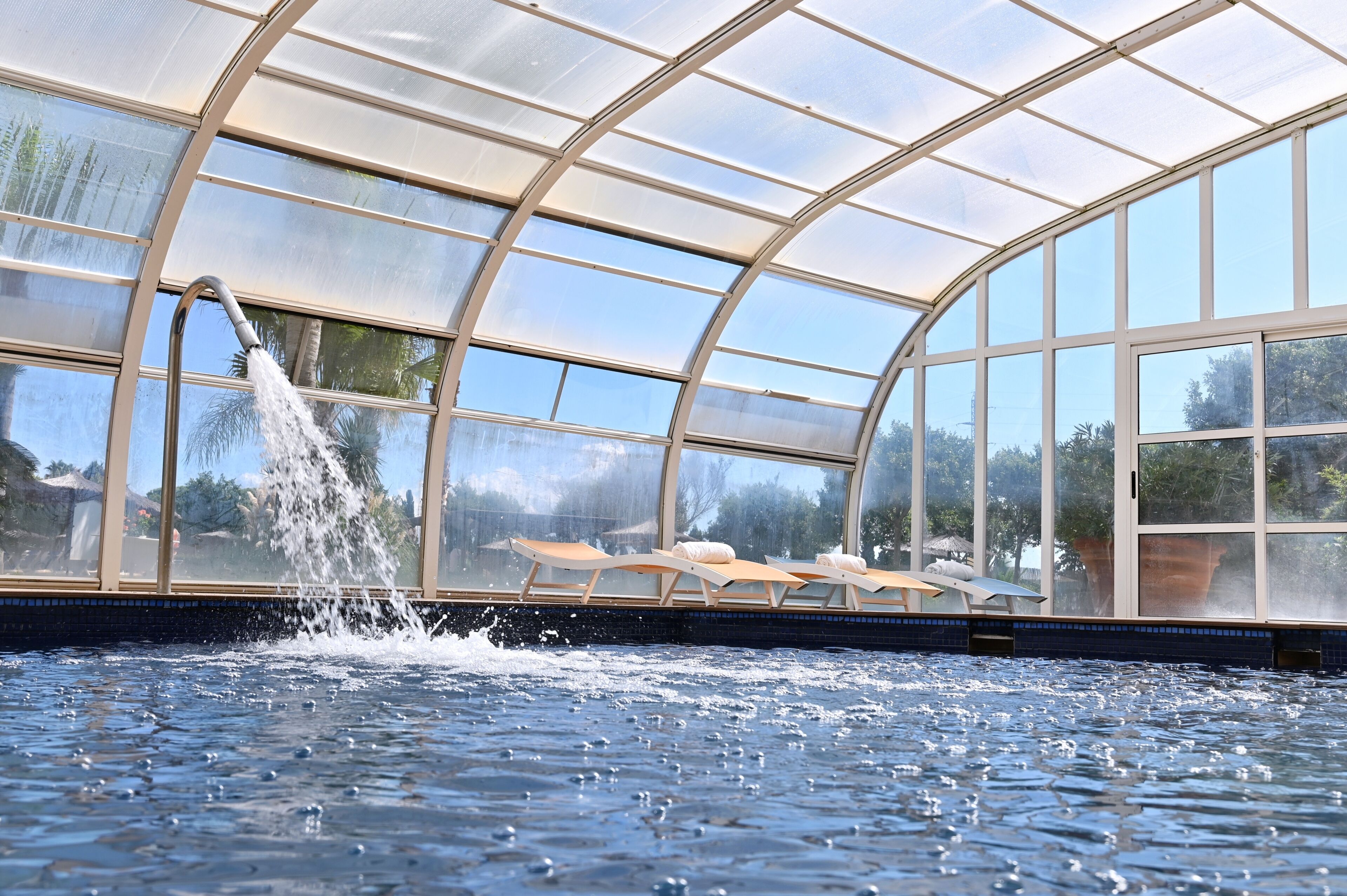 Area piscina con tetto in vetro, poltrone relax e fontana.