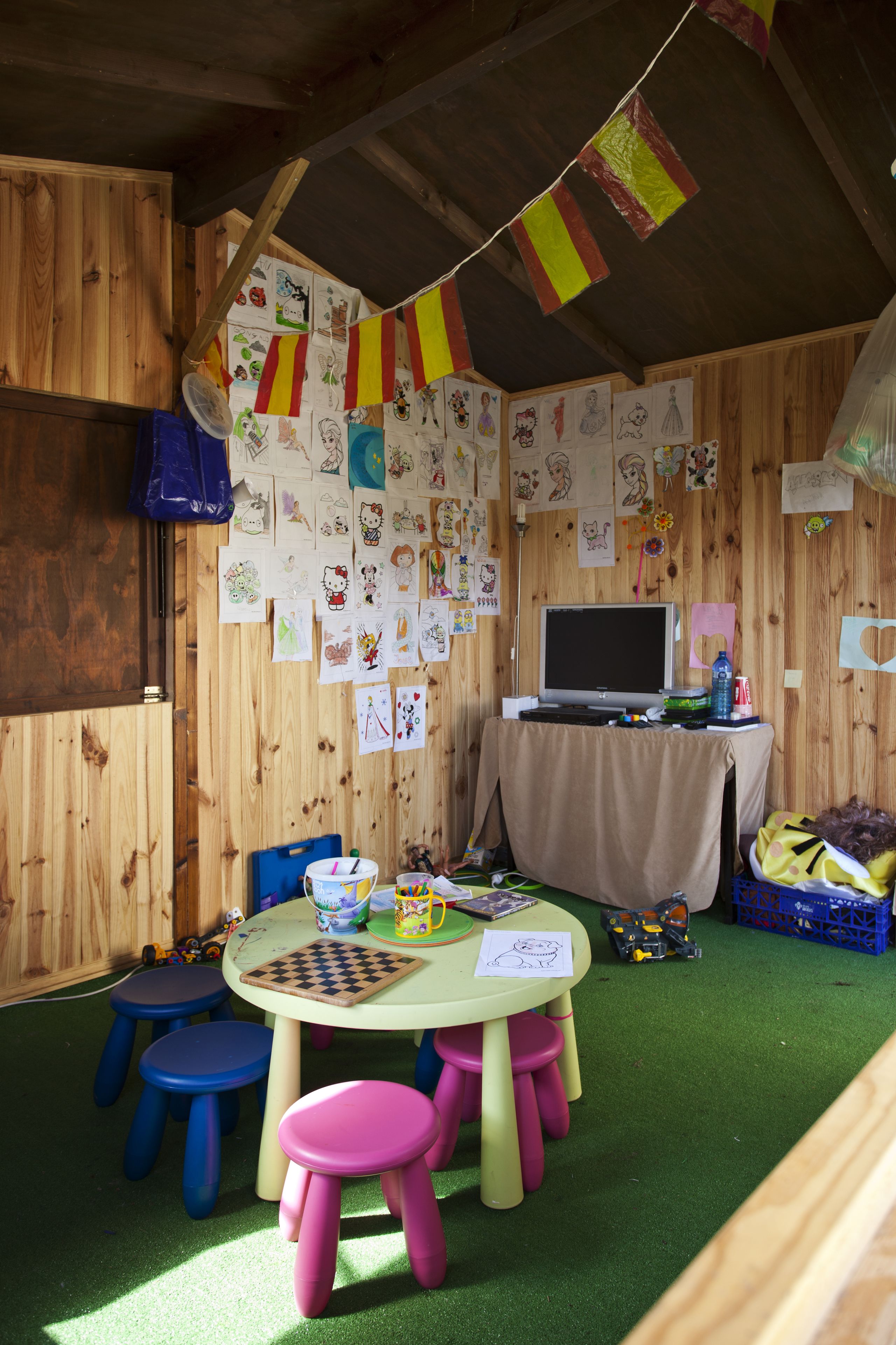 A children's playroom with a wooden interior, a round table with a laptop, and colorful artwork on the walls.
