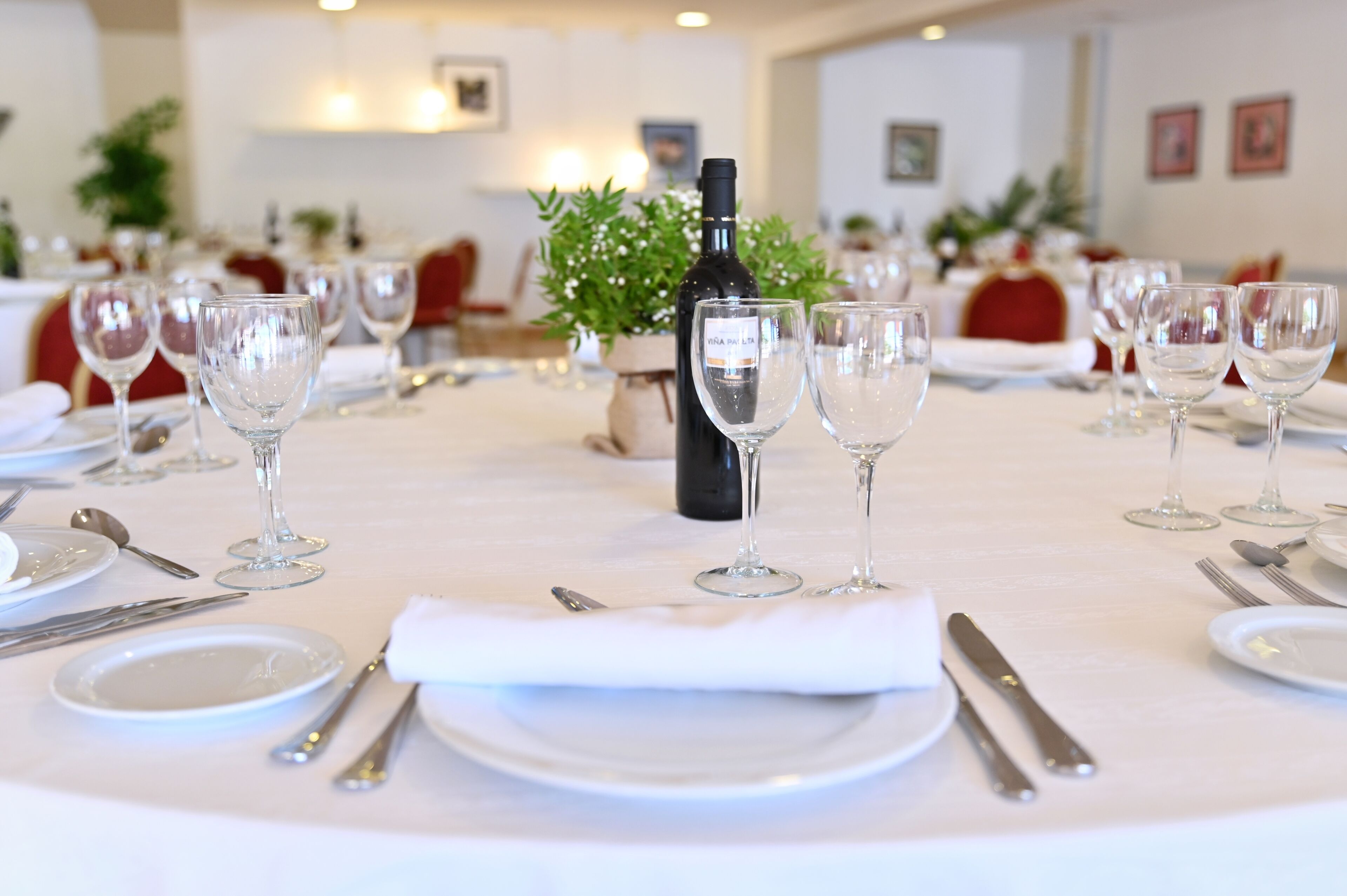 A dining table set with wine glasses, plates, and cutlery, with a bottle of wine in the center.