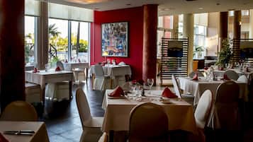 Un restaurant avec des tables dressées, de grandes fenêtres et un mur d’accent de couleur rouge.