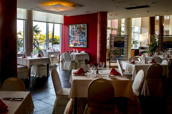 Un restaurante con mesas dispuestas para comer, ventanas amplias y una pared de acento roja.
