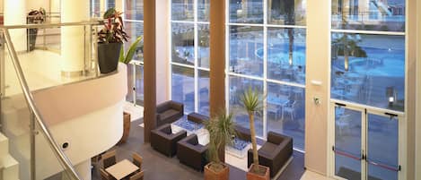 A spacious lobby with a high ceiling, large windows, and a view of the outdoor pool area.