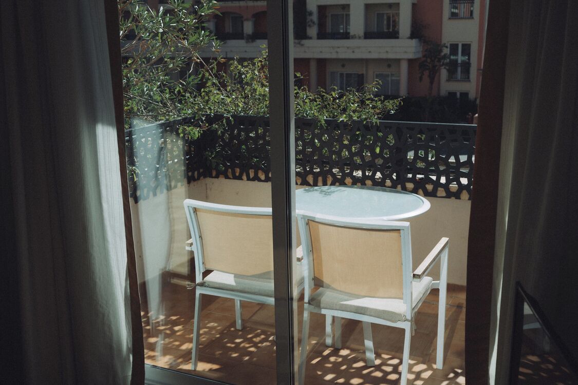 Un balcon avec une table ronde et deux chaises, une clôture en métal noir et un bâtiment en arrière-plan.