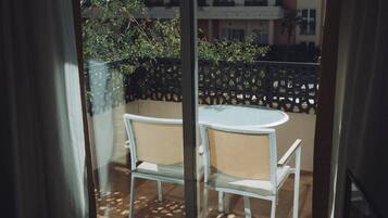 A balcony with a round table and two chairs, a black metal fence, and a building in the background.