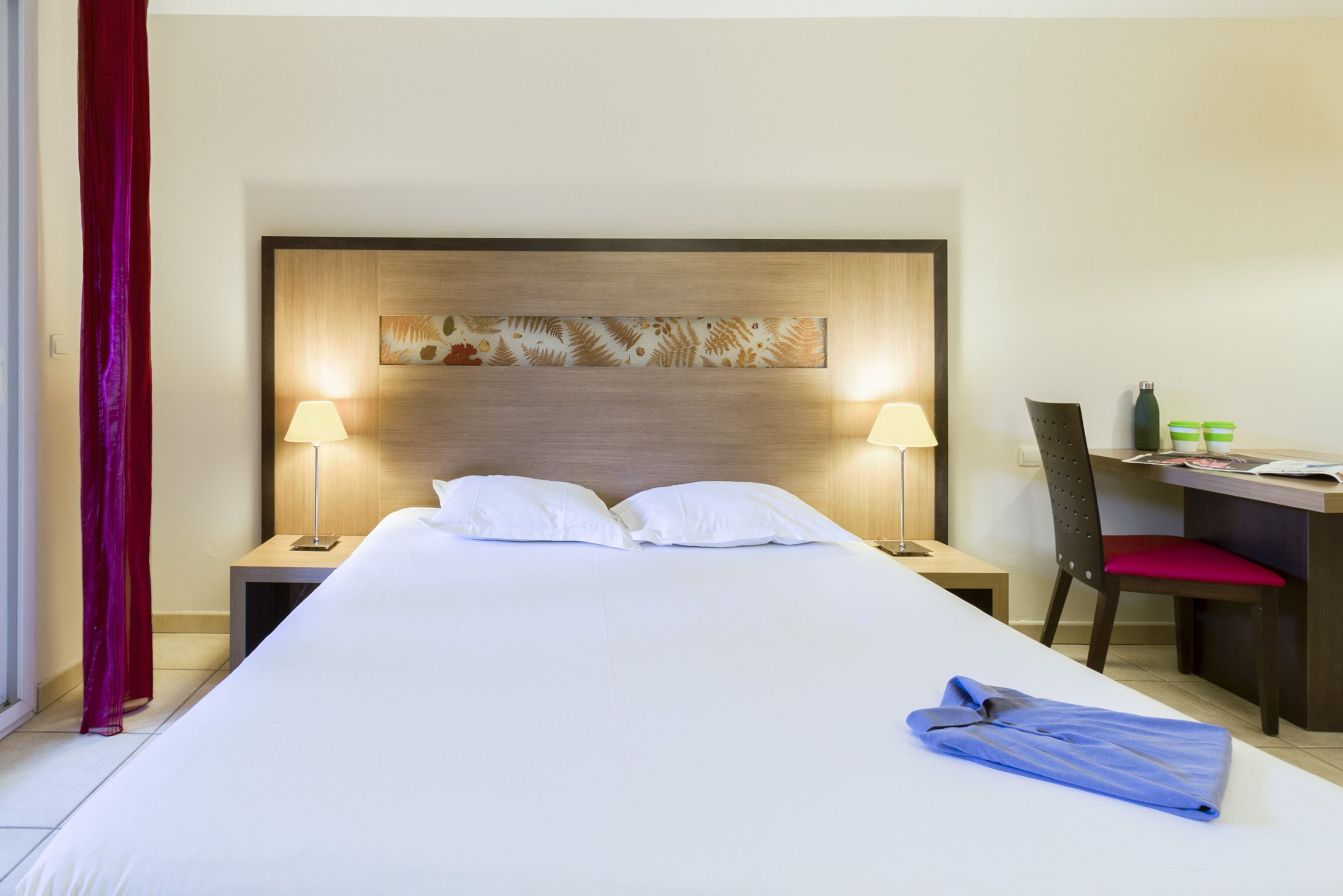 Une chambre d’hôtel avec un grand lit, deux lampes de chevet, un bureau avec une chaise et une tête de lit décorative.