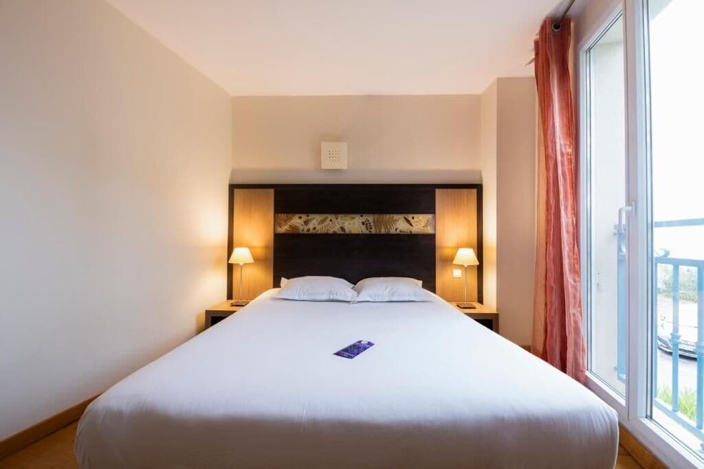 Ein Hotelzimmer mit Bett, Nachttischen, Lampen, einem Vorhang und einem Fenster mit Ausblick.